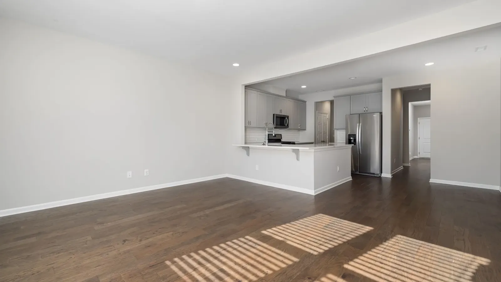 Bright, empty apartment living room with hardwood floors and an open kitchen